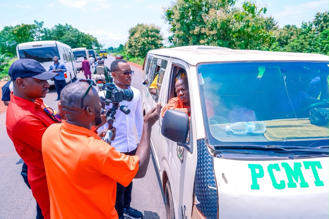 Motorists - The Times of Abuja Group of men filming a white van labeled PCMT on a rural road, with bystanders and green trees in the background.