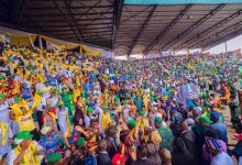 Large crowd at a stadium rally with yellow and green attire, banners, and waving scarves.