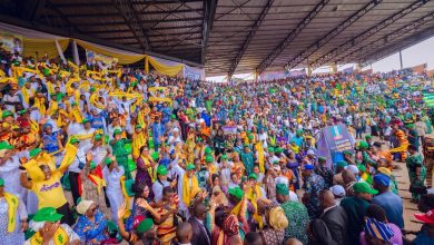 Large crowd at a stadium rally with yellow and green attire, banners, and waving scarves.