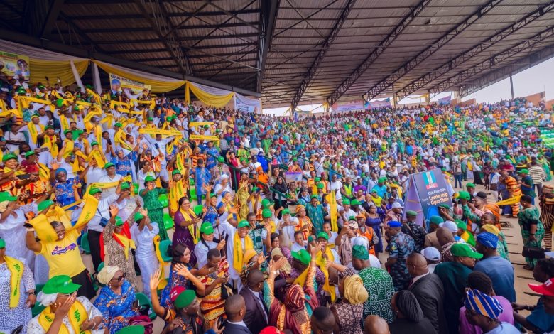 Large crowd at a stadium rally with yellow and green attire, banners, and waving scarves.