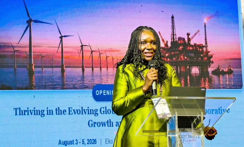 Oritsemeyiwa Eyesan - The Times of Abuja Female speaker in lime-green attire presenting at a conference, with wind turbines and an offshore oil-rig backdrop at sunset.