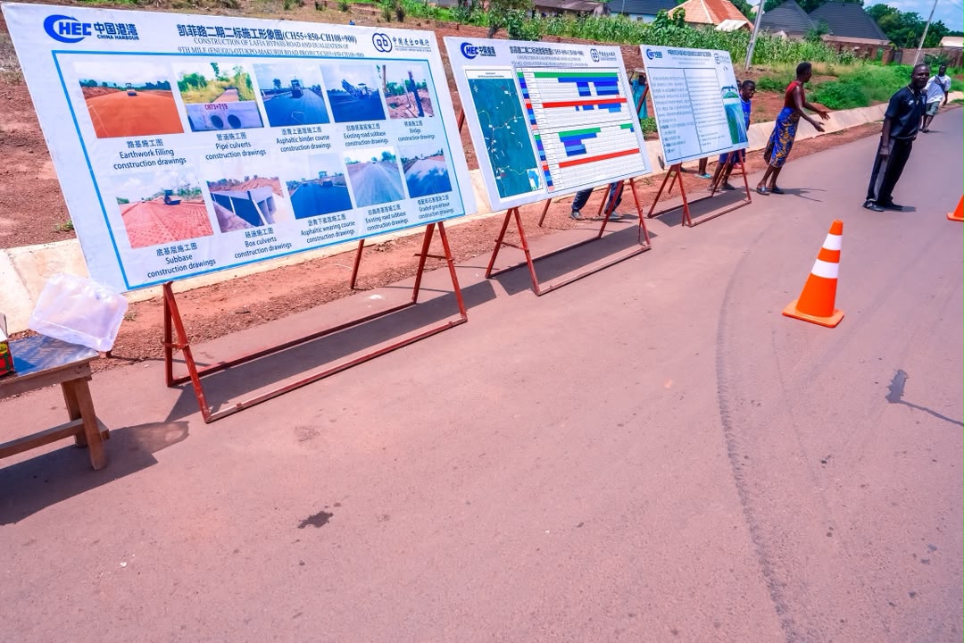 Road construction - The Times of Abuja Row of large construction project boards on metal stands placed along a paved road, with photos, diagrams, and charts for public viewing.