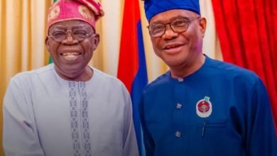 Two men in traditional Nigerian attire smile for the camera, with colorful flags behind them.