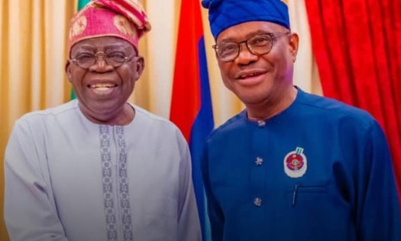 Two men in traditional Nigerian attire smile for the camera, with colorful flags behind them.